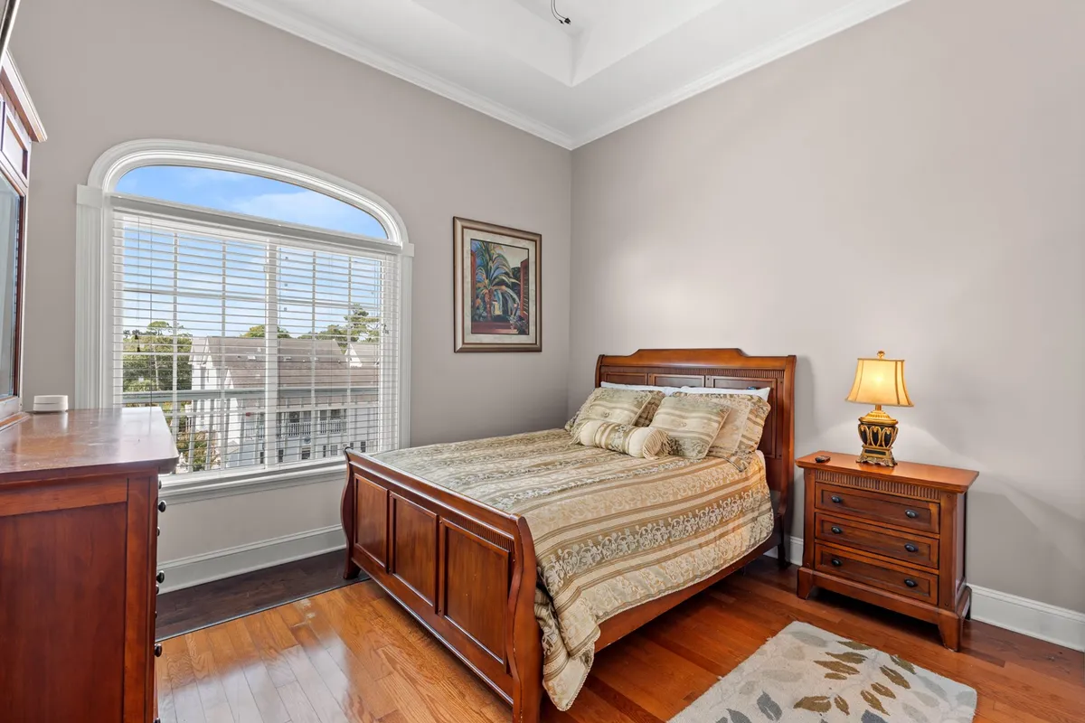 A sunlit bedroom featuring a bed with decorative pillows, wooden furniture, and a window that opens up to gentle daylight. The space is styled warmly, blending comfort with an inviting sense of relaxation, ideal for a quiet morning retreat.