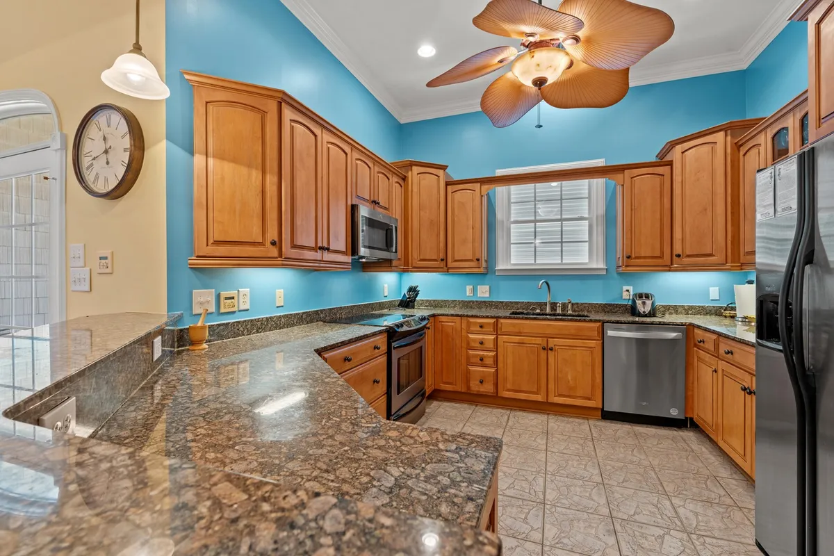 Featuring a welcoming kitchen space with granite countertops, wooden cabinets, cheerful blue wall paint, and a ceiling fan, this image highlights the well-equipped kitchen perfect for preparing meals and entertaining guests. The layout suggests convenience and comfort for cooking and socializing.