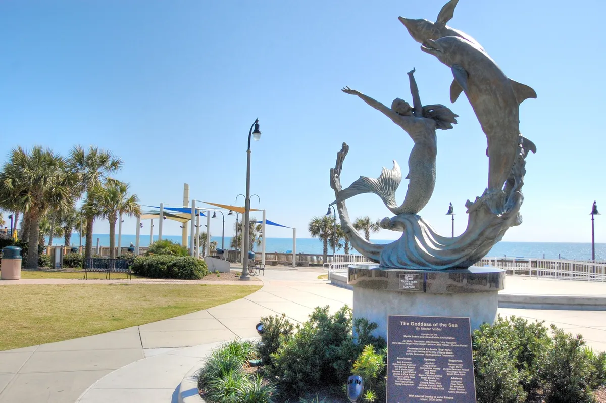 A striking statue of the Goddess of the Sea stands along a pathway with palm trees and sweeping ocean views. The scene radiates a celebratory, relaxed vibe, inviting guests to stroll the beachfront, take memorable photos, and soak in the coastal atmosphere. The pathway hints at easy access to local attractions and a sense of exploration.