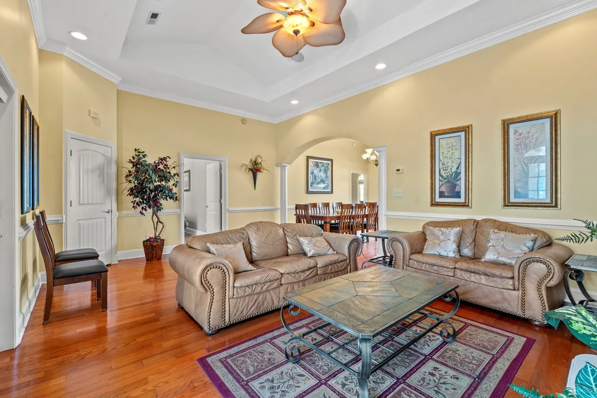 The image showcases a warm, inviting living room with plush leather sofas, a decorative coffee table at the center, and tasteful artwork adorning the walls. The setup is perfect for relaxing, socializing, or gathering with family and friends after a day at the beach.