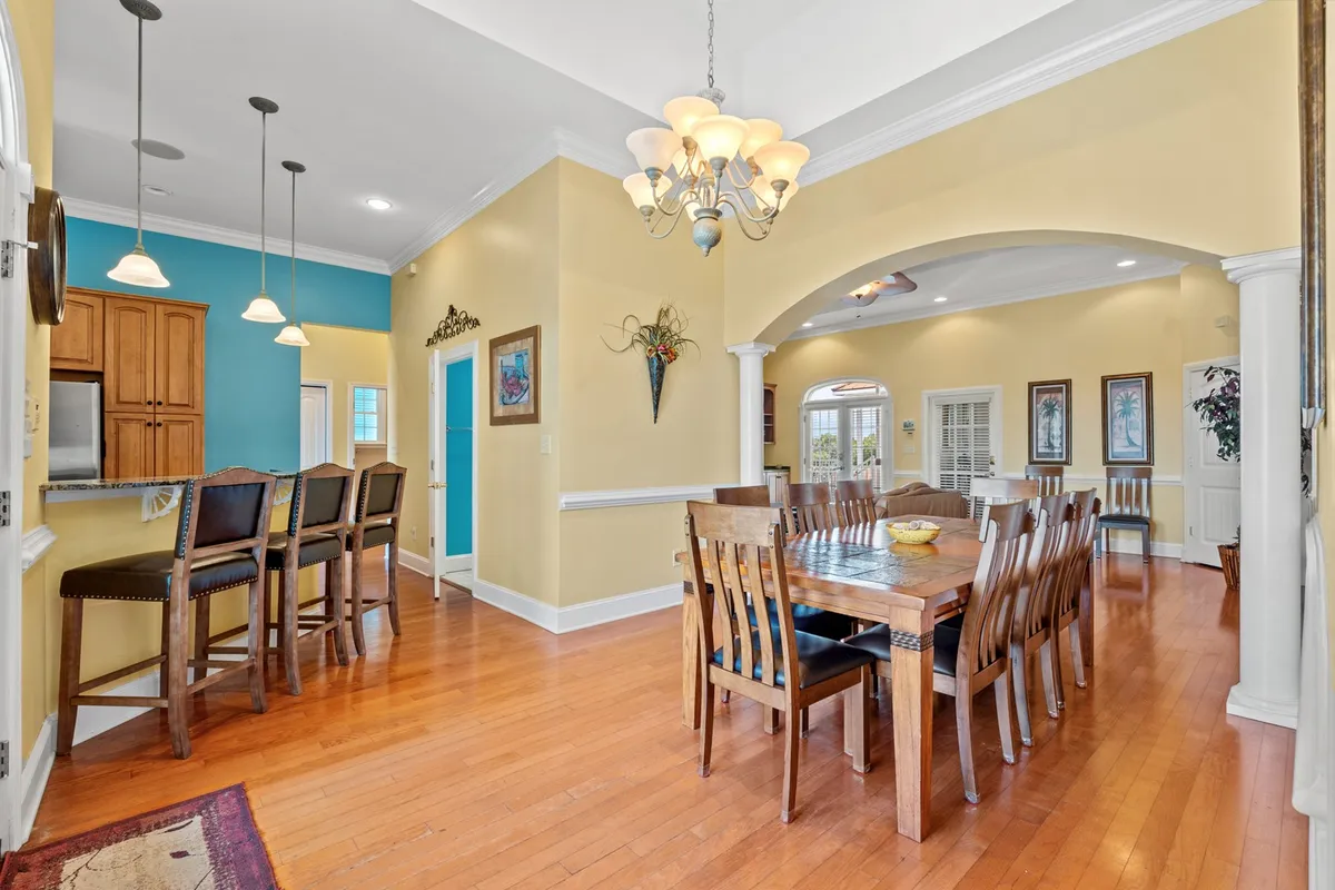 This image showcases a bright, inviting dining area featuring a central dining table complemented by a kitchen bar, a striking blue accent wall, a chandelier overhead, and an arched doorway. The setup is perfect for family meals and gatherings, and the open layout allows for easy interaction between the kitchen and dining spaces.