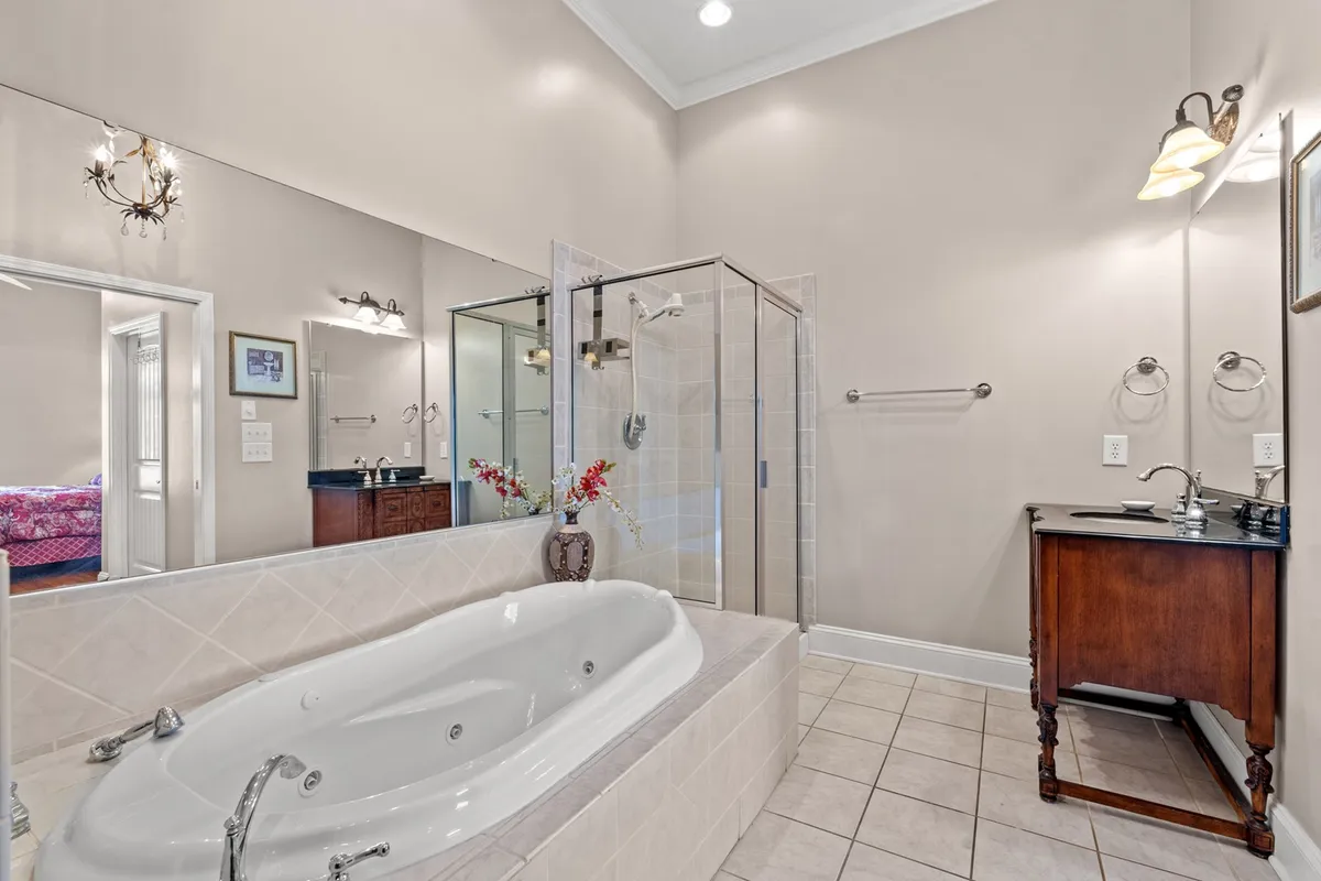 A modern bathroom with a luxurious jacuzzi tub, glass shower enclosure, sleek vanity with sink, and decorative touches like fresh flowers. The space exudes a spa-like ambiance, ideal for relaxation and self-care.