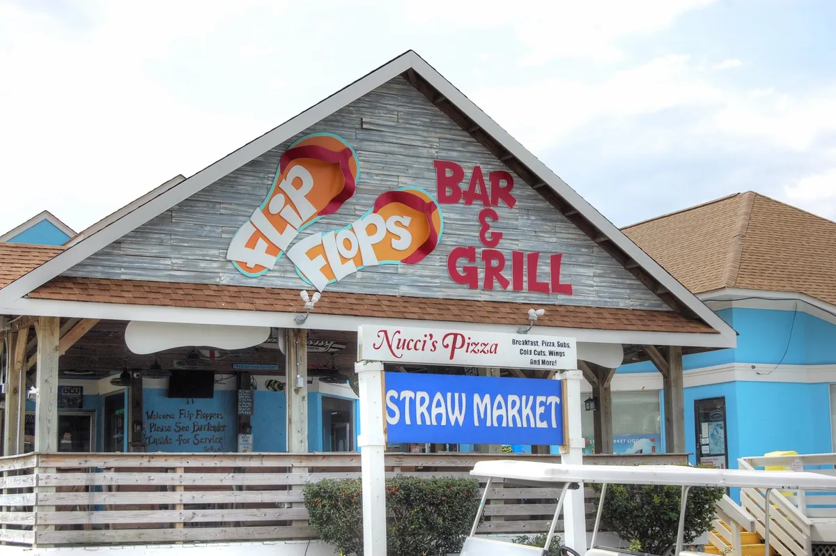 A snapshot of bustling vacation life with signs for local eateries and shops, including Flip Flops Bar & Grill, Nucci's Pizza, and the Straw Market. The image conveys a sense of lighthearted fun and the abundance of nearby dining and shopping options.