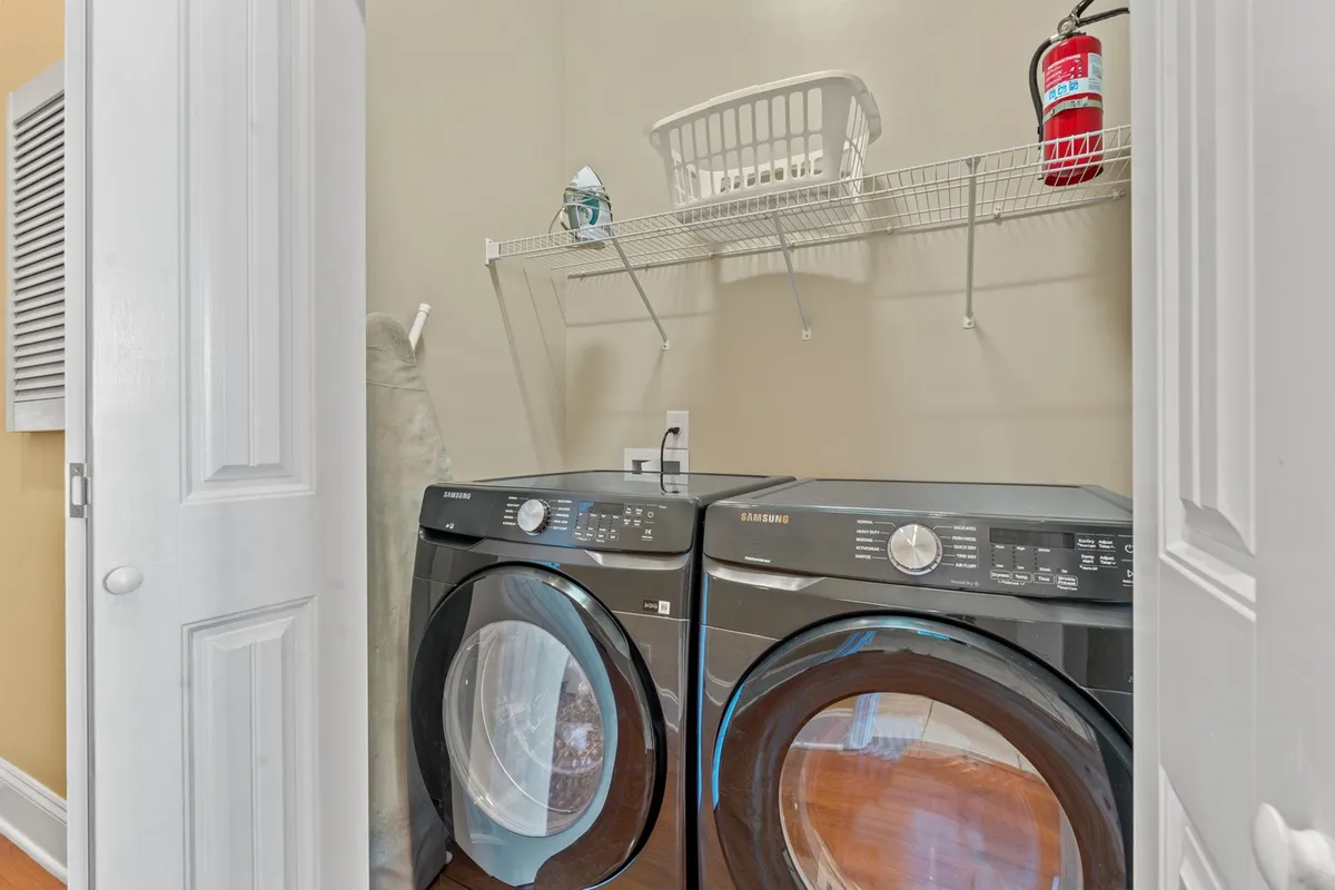 A practical laundry area featuring a washer and dryer, a laundry basket, and a shelf with cleaning supplies. The organized, functional design emphasizes ease and convenience for families or groups.