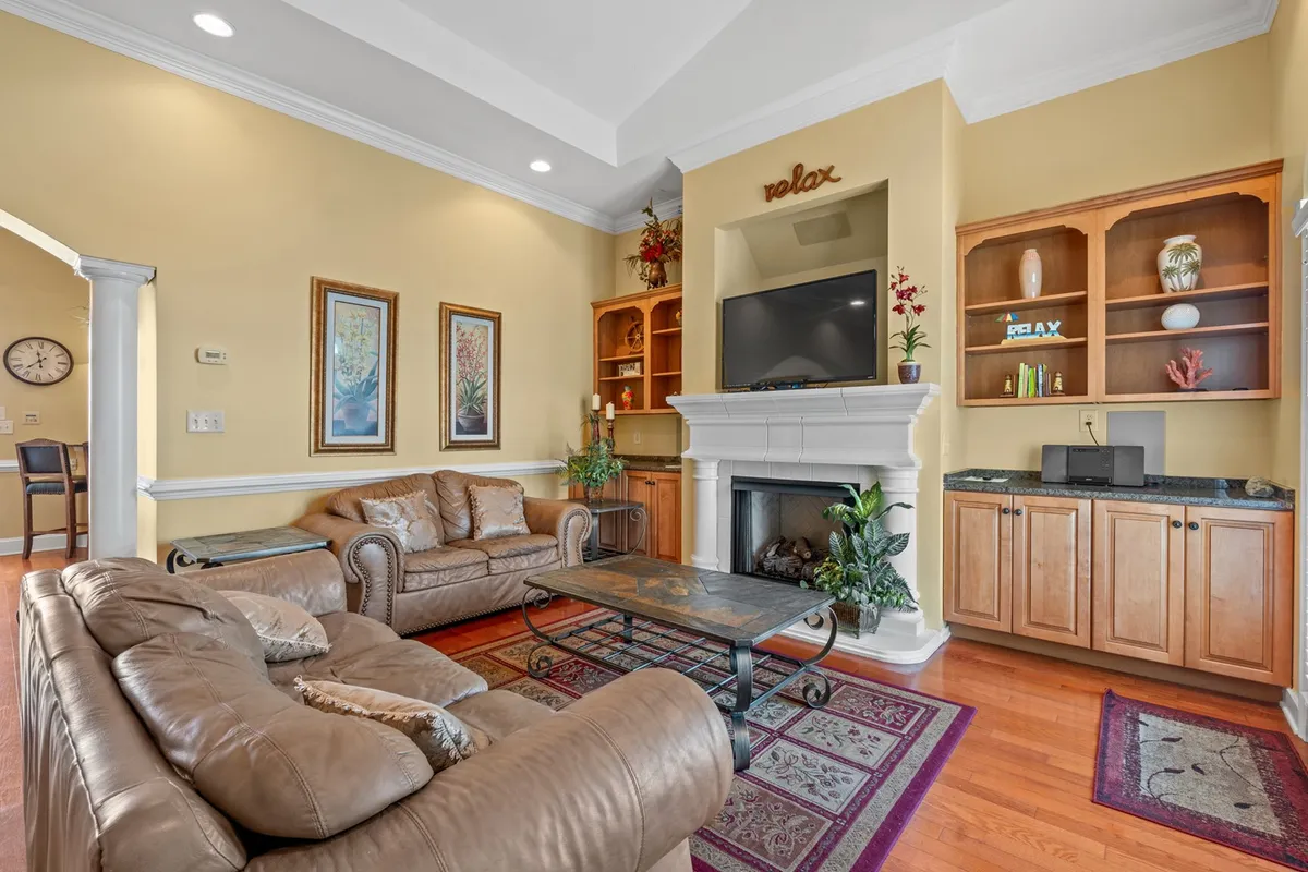 A warm, inviting living room featuring comfortable leather couches arranged around a decorative coffee table and a fireplace with a mantle. A television is mounted above the fireplace, creating a cozy spot for family movie nights or sharing stories. Soft lighting and tasteful decor make the space feel welcoming and perfect for gatherings.